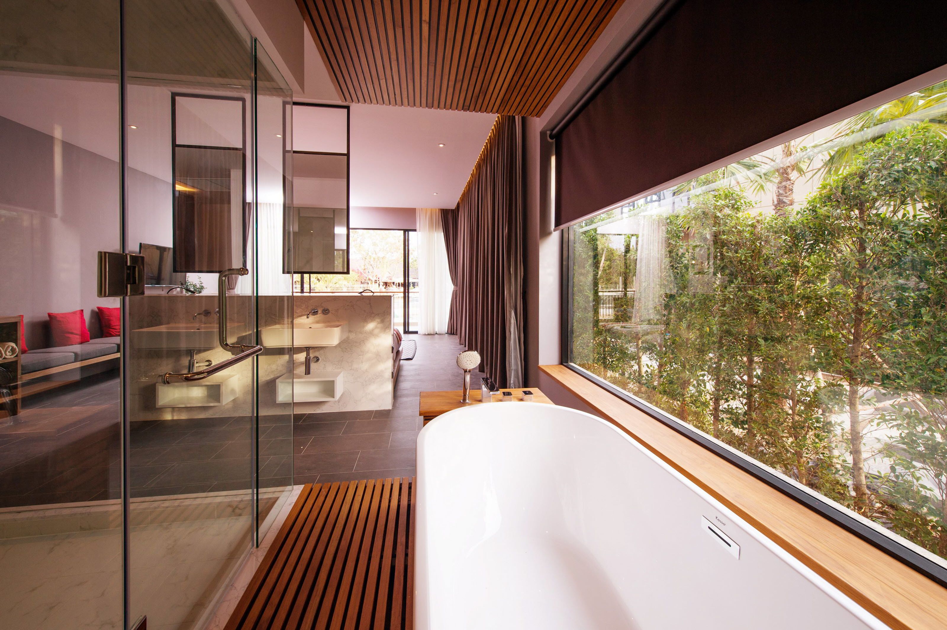 A modern bathroom with a large bathtub, a glass shower enclosure, and a view of greenery outside.