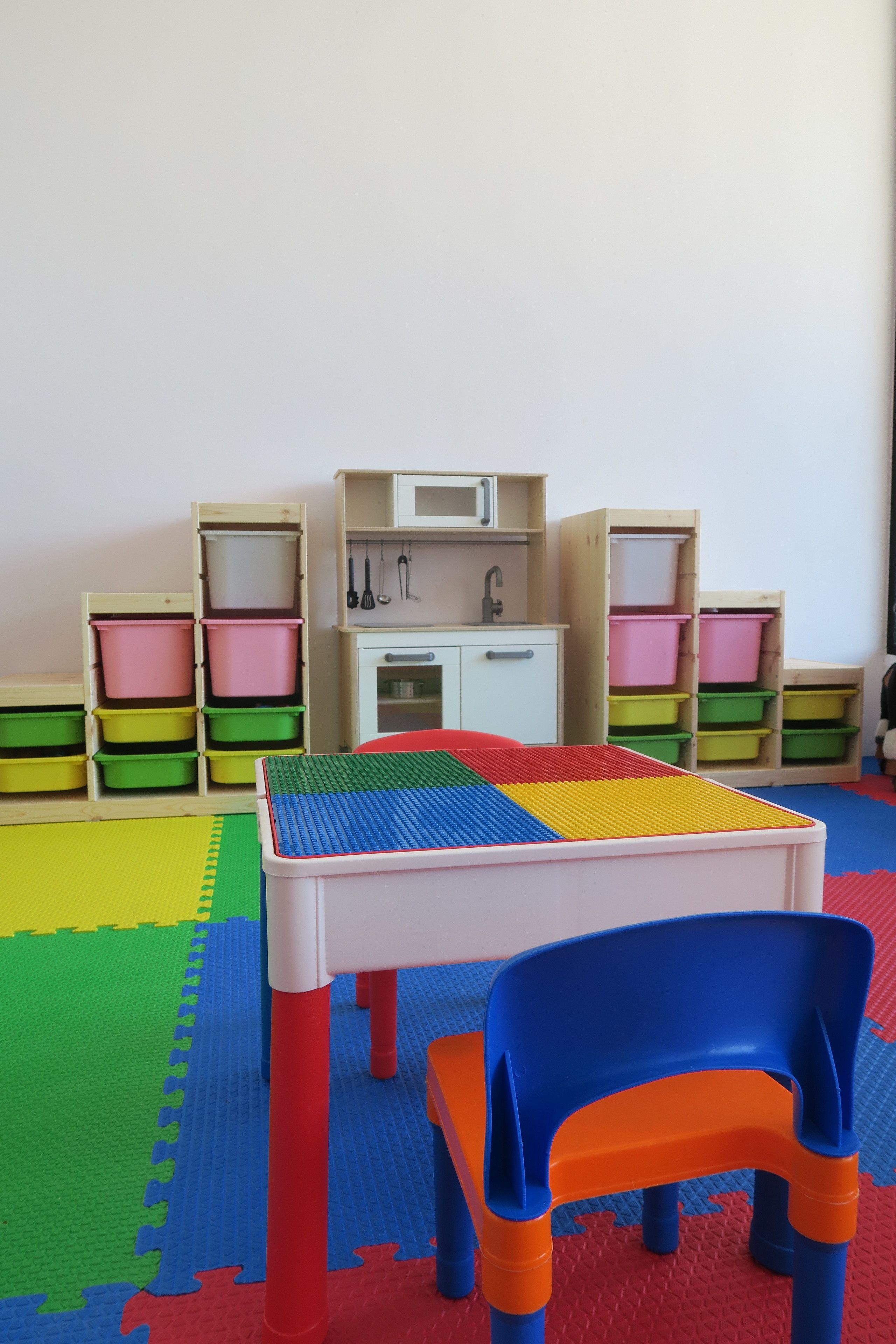 Un área de juegos con mesa y sillas, contenedores de almacenamiento y una kitchenette.