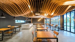 A modern dining area with wooden tables and chairs, a marble counter, and large windows offering a view of the outdoors. - The Gallery Hotel Nai Harn (Rawai)