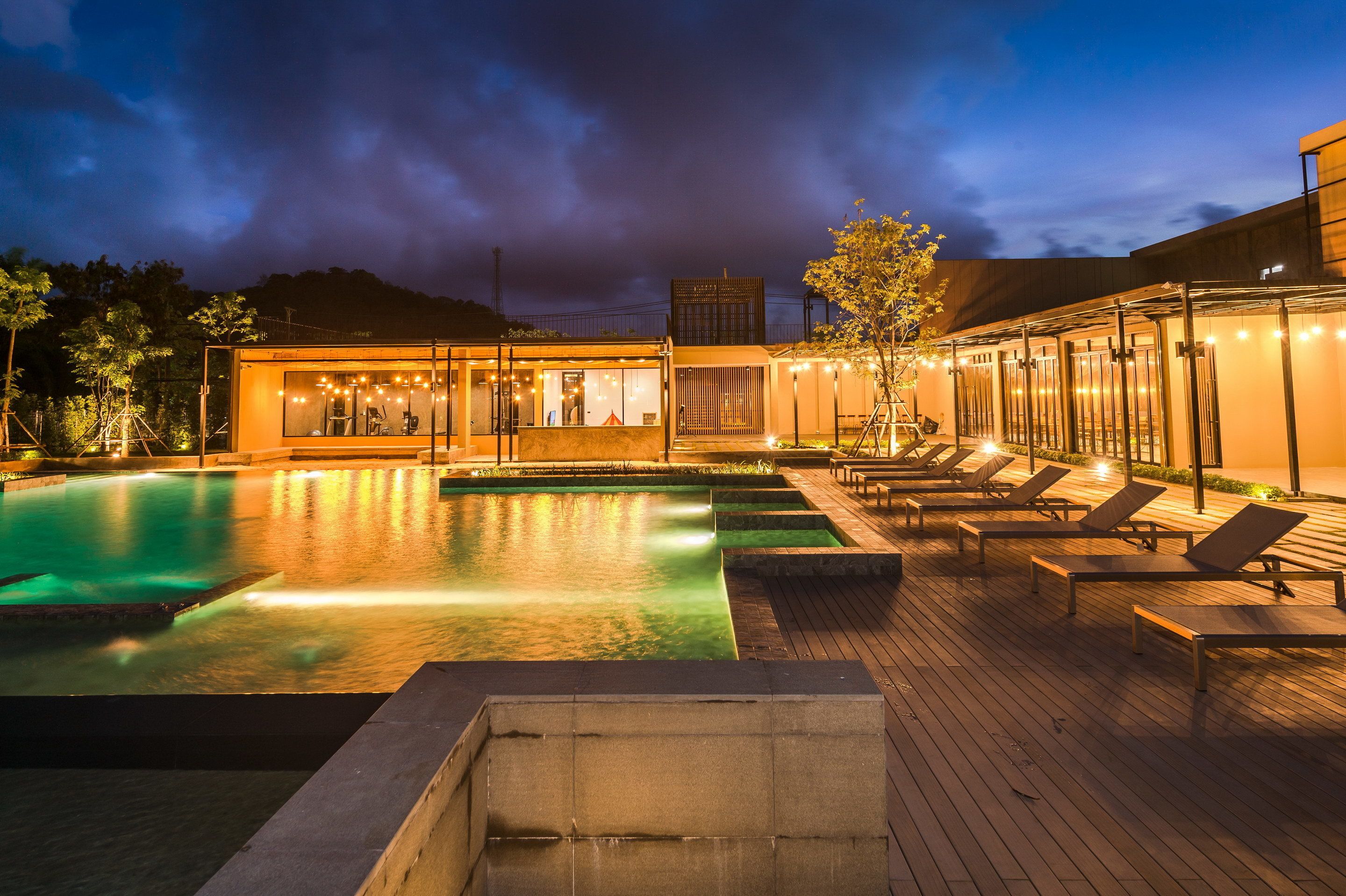 A pool area with lounge chairs and a building with glass walls.