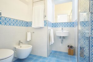 A bathroom with a white toilet, a white bidet, a glass shower enclosure, and a sink with a mirror above it. - Palazzo Gentilcore (Castellabate)