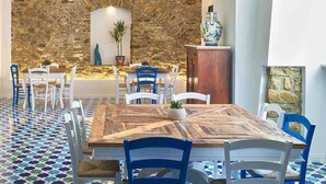 A dining area with a rustic wooden table, white and blue chairs, a stone wall, and a tiled floor. - Palazzo Gentilcore (Castellabate)