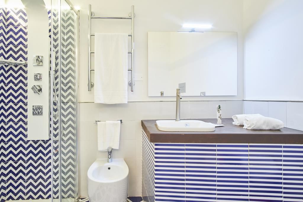 Un baño moderno con ducha, lavamanos, espejo y baldosas a rayas.