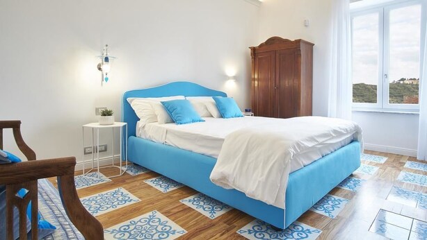 A bedroom with a bed, a nightstand, a wooden wardrobe, and a window with a view. - Palazzo Gentilcore (Castellabate)