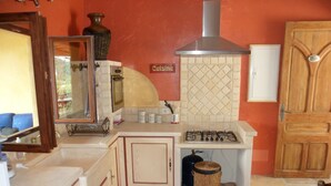 A compact kitchen with a gas stove, a microwave, and a sink. There is a wooden door and a small trash bin. - Les Gites du Lac - Chambre d'hotes (Montauroux)