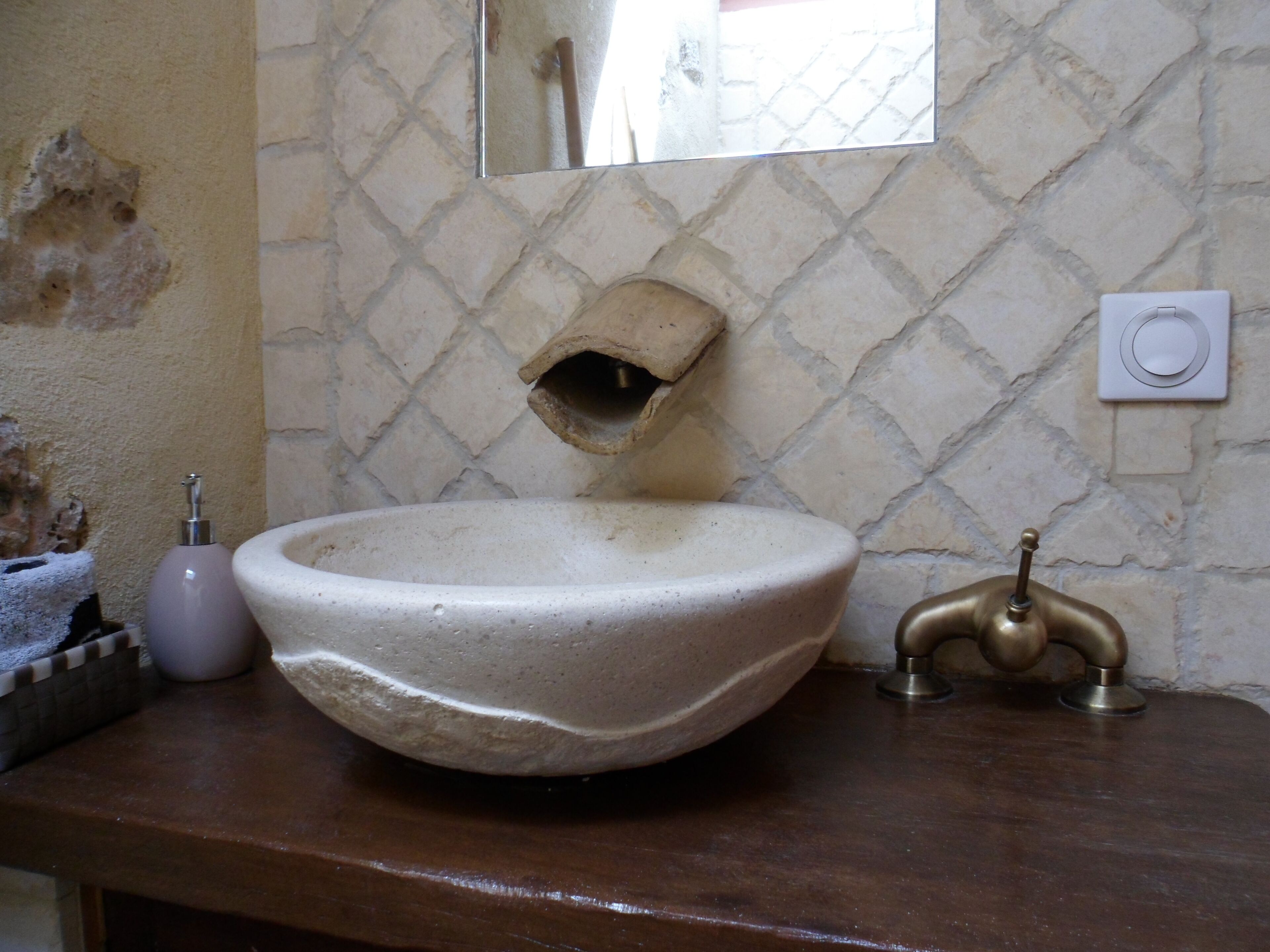 Un baño con un lavamanos grande, redondo y color beige, un grifo de latón y un espejo encima.