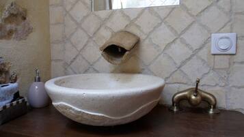 Un baño con un lavamanos grande, redondo y color beige, un grifo de latón y un espejo encima.