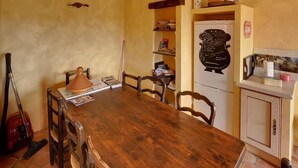 A dining area with a wooden table, chairs, a Moroccan tagine, and a bookshelf. - Les Gites du Lac - Chambre d'hotes (Montauroux)