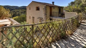 A stone house with a tiled roof, a balcony, and a view of a hilly landscape. - Les Gites du Lac - Chambre d'hotes (Montauroux)
