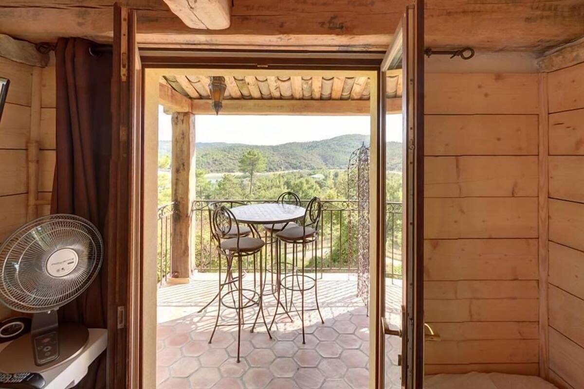 Une cabane en bois dotée d’un balcon avec une table et des chaises, un ventilateur et une vue sur un paysage montagneux.