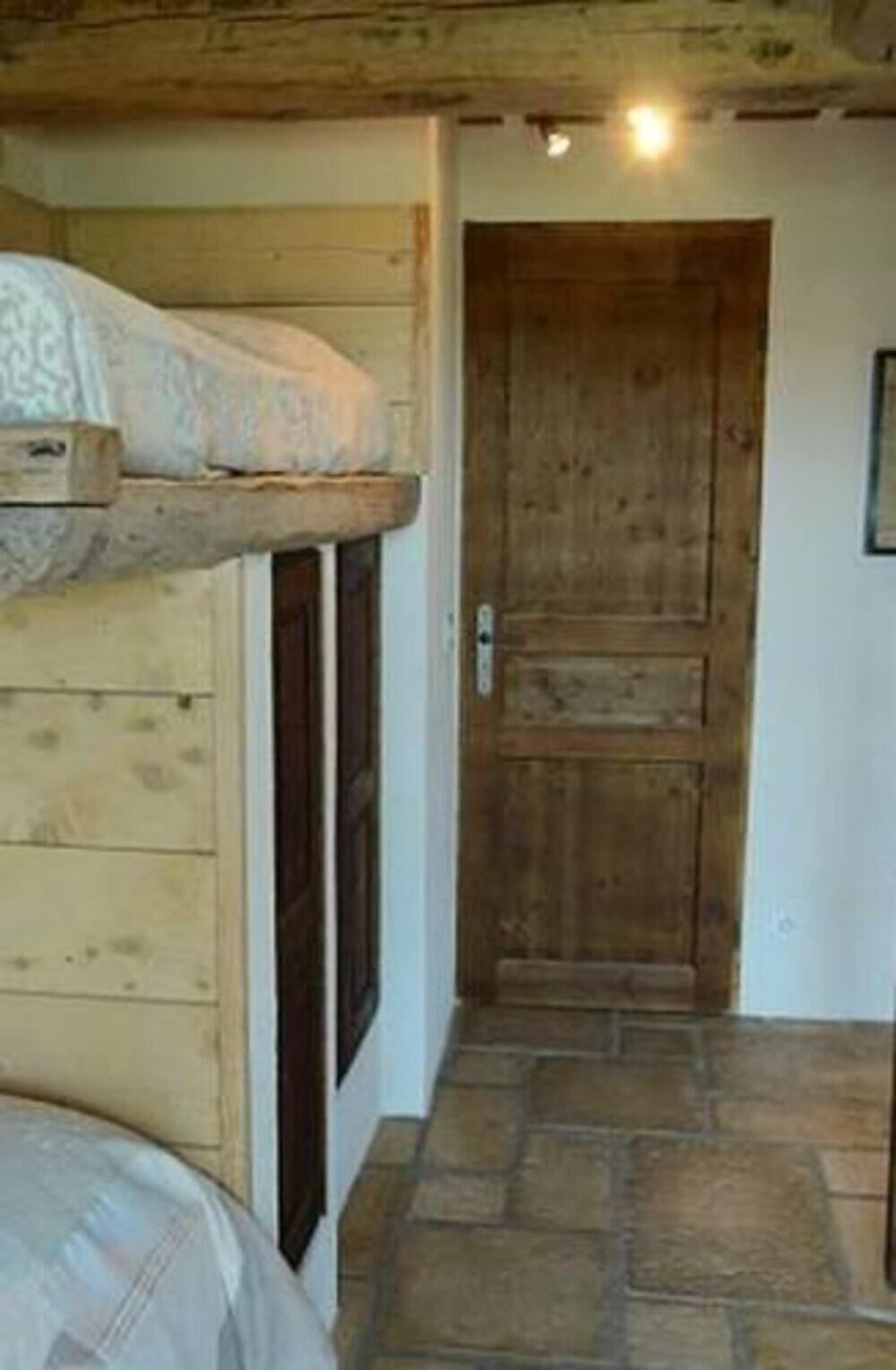 A wooden room with a stone floor, a wooden door, and a bed with a white bedspread.