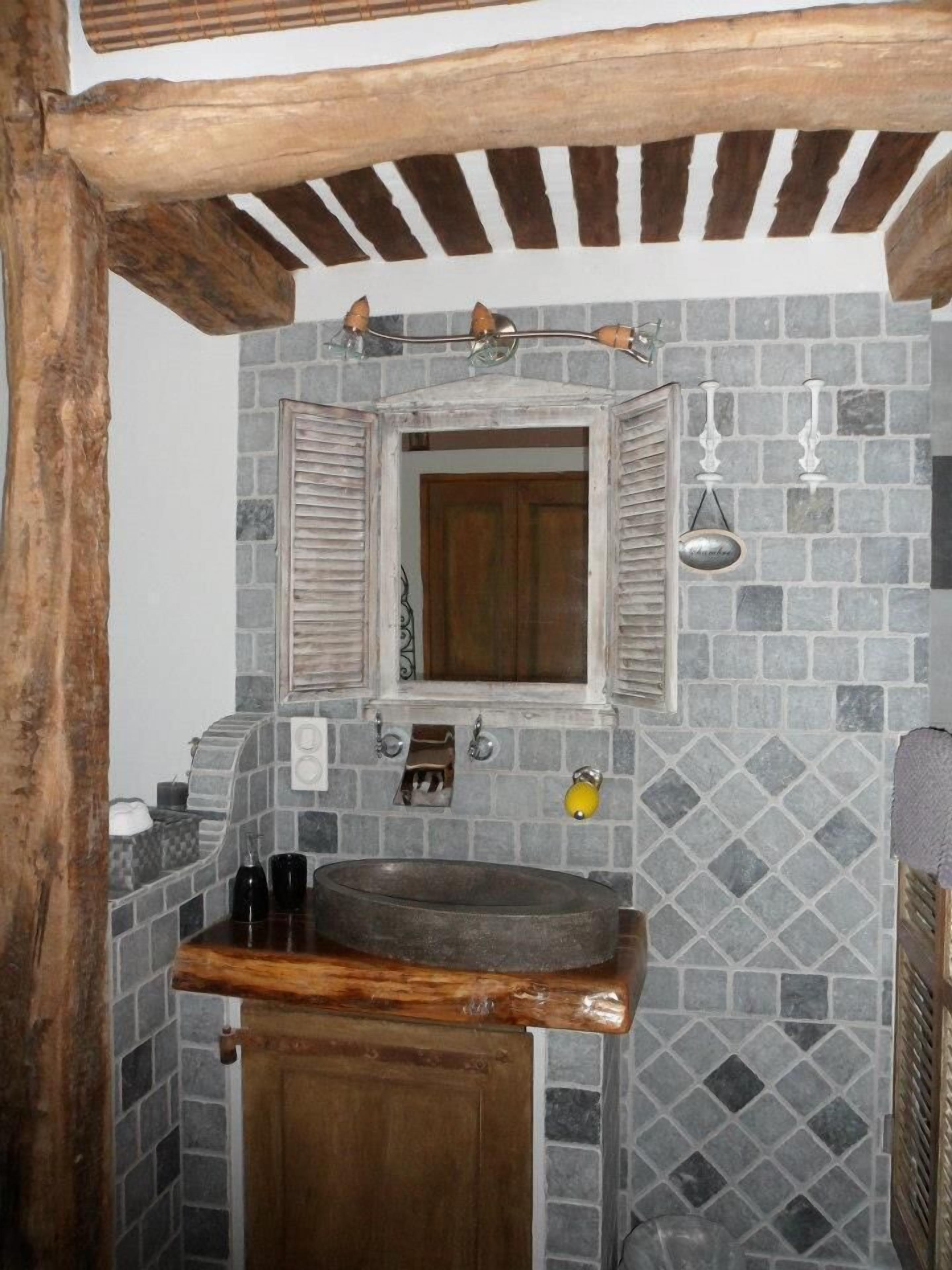 Un baño rústico con pared de baldosas de piedra, lavabo de madera y puerta de madera.