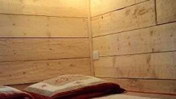 Une petite pièce chaleureuse aux murs en bois, avec un lit simple recouvert d’une courtepointe.