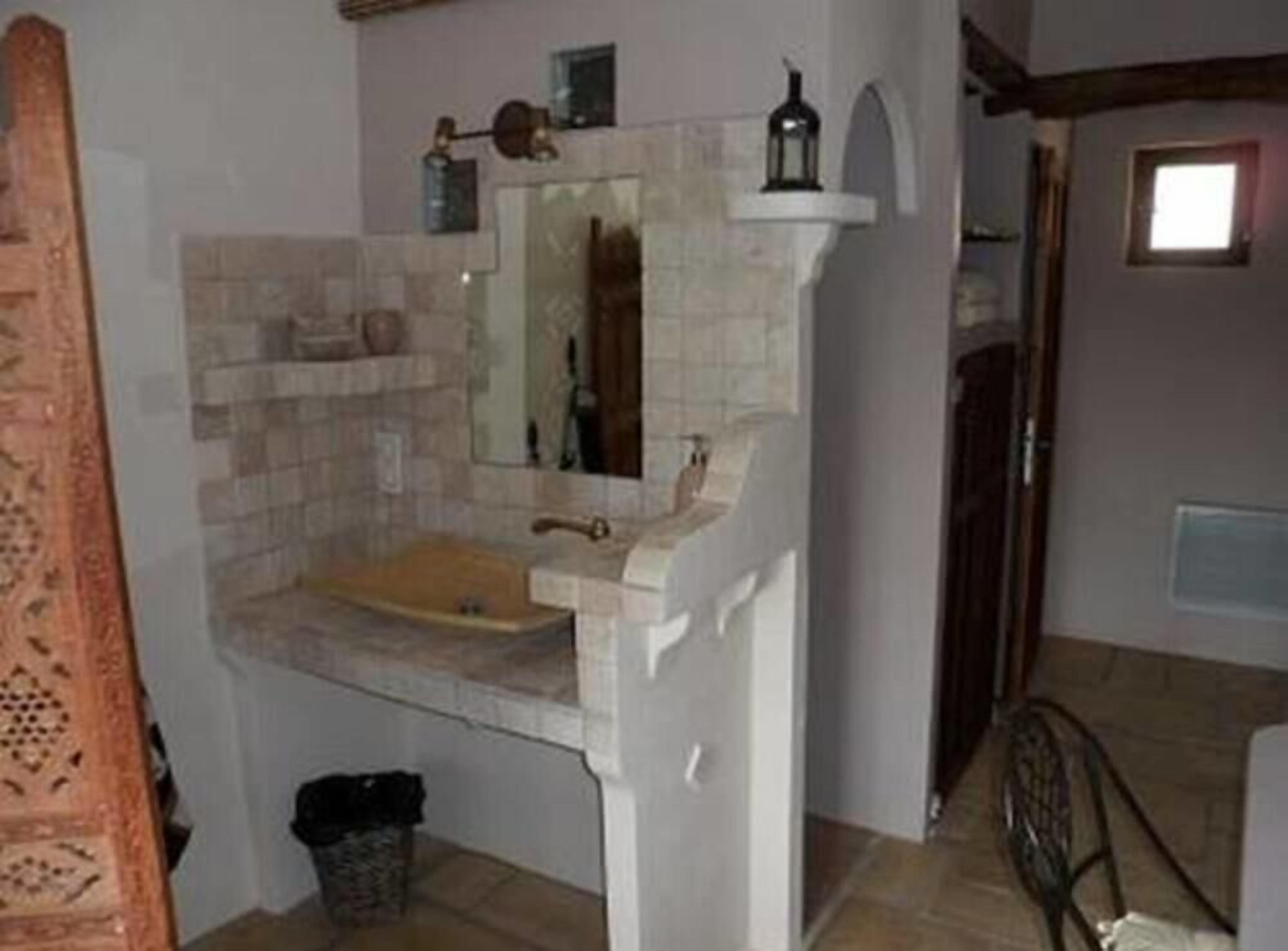 Un baño con lavamanos, espejo y un pequeño estante con artículos de aseo.