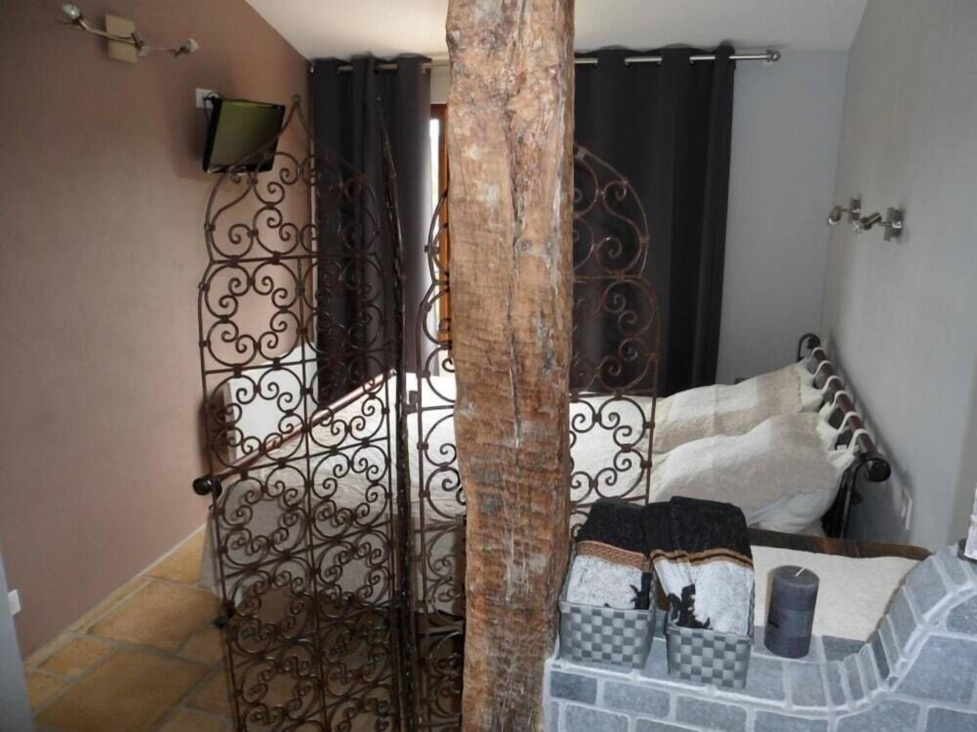 A bedroom with a bed, a stone wall, a metal gate, and a small table with a candle.