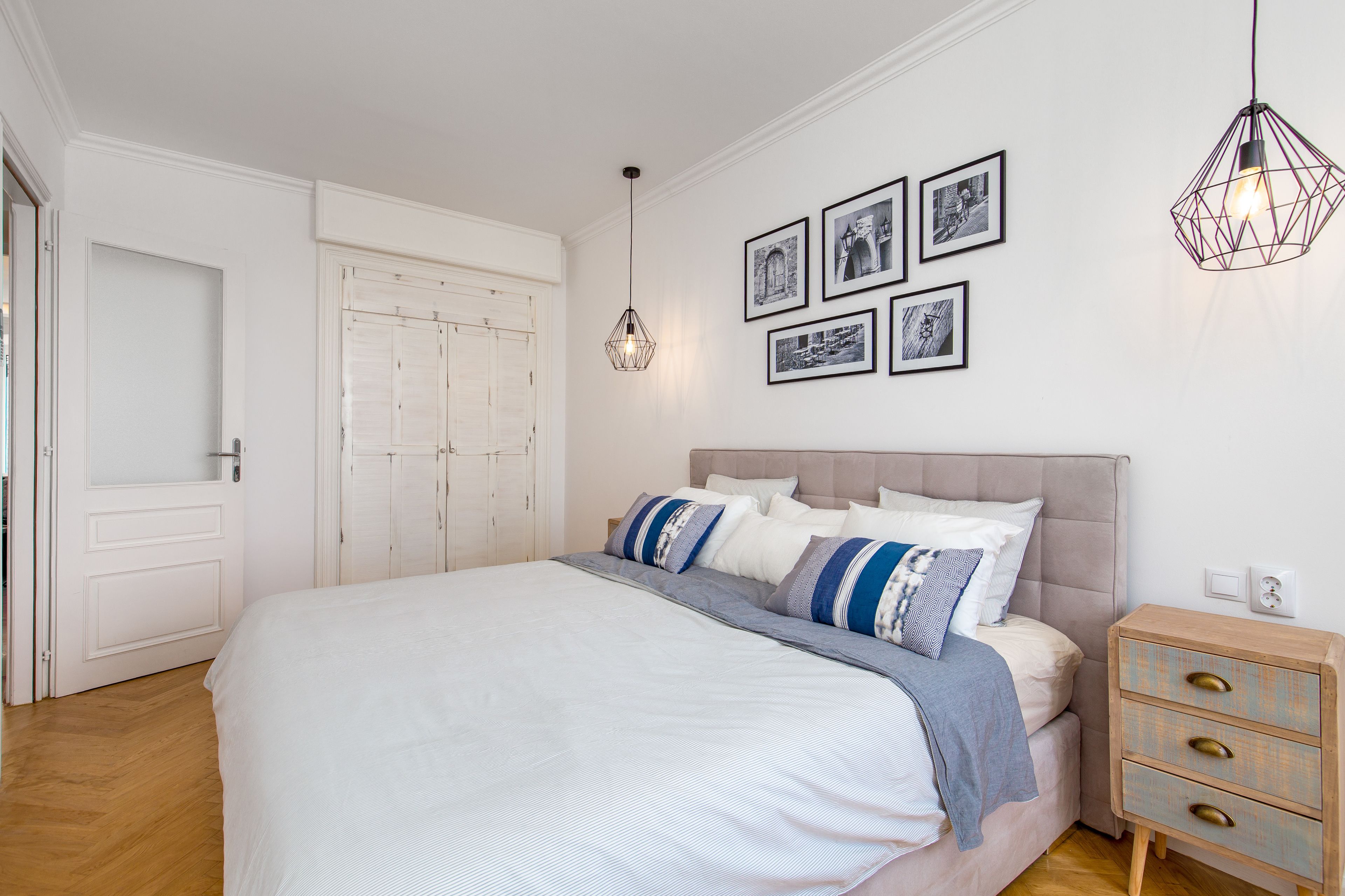 A bedroom with a large bed, a nightstand, a hanging light fixture, and framed pictures on the wall.
