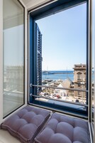 Una ventana con vistas a un puerto deportivo, un edificio con balcón y un área de estar con cojines.
