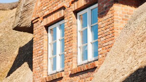 A brick building with two windows and a black lantern. - Hotel Aarnhoog (Sylt)