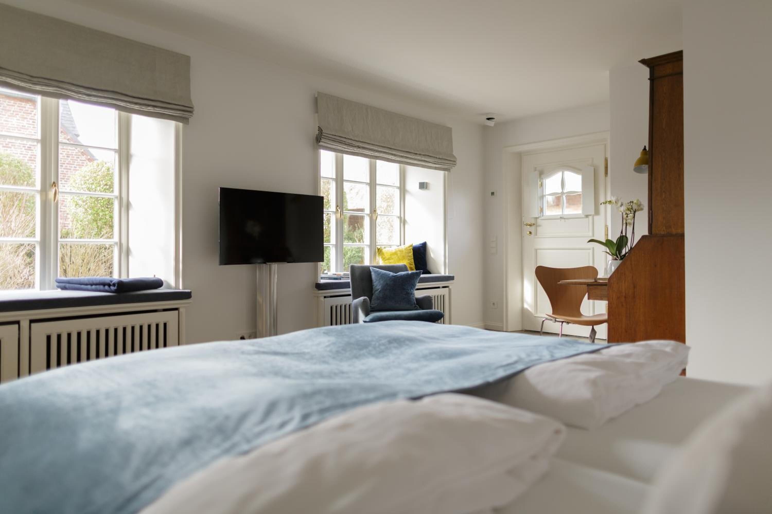 A bedroom with a bed, a TV, a chair, and a desk.