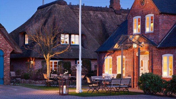 A traditional building with a thatched roof and brick exterior, featuring outdoor seating and a well-lit entrance. - Hotel Aarnhoog (Sylt)
