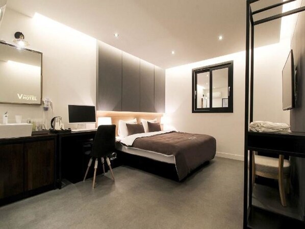 A modern hotel room with a bed, desk, and chair, a large mirror, and a television. - V Hotel (Busan)