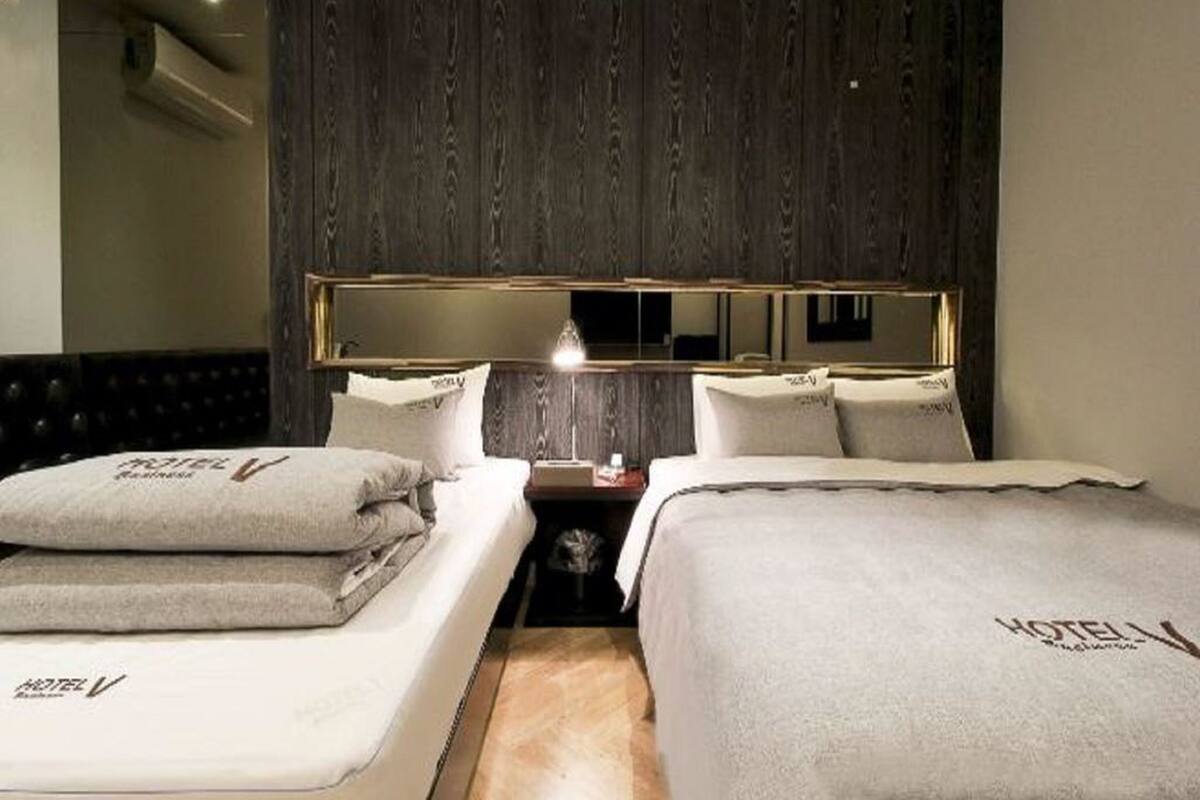 A hotel room with two beds, a wooden headboard, a nightstand with a lamp, and a large mirror.