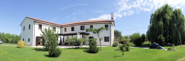 A two-story building with a red-tiled roof, a covered patio area, and a well-maintained lawn with several trees.