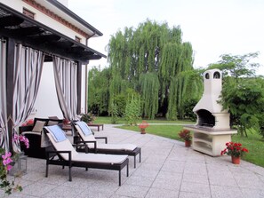 An outdoor patio with lounge chairs, a pergola, and a stone oven.