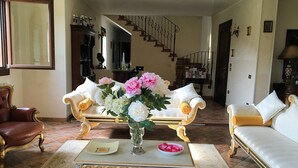 Uma sala de estar espaçosa com uma escadaria imponente, móveis elegantes e um vaso de flores sobre uma mesa de centro.