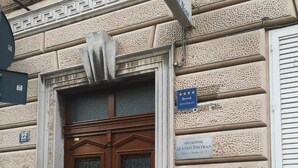 Entrada d'un edifici amb una porta doble de fusta, una placa que indica que és un apartament i un cartell d'un restaurant proper.