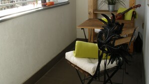 Un balcó amb taula de fusta, cadires, una guitarra i una planta en test.
