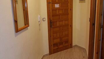 Un couloir avec une porte en bois, un miroir et un interrupteur sur le mur.