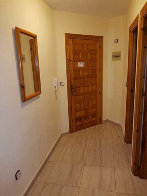 A hallway with a wooden door, a mirror, and a light switch on the wall.