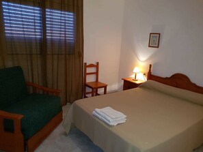 A hotel room with a bed, a chair, a nightstand with a lamp, and a window with blinds.
