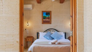A bedroom with a bed, pillows, a bedside table, and a wall-mounted painting. - Ta Danjela Villa Sleeps 8 With Pool (Xaghra)