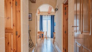 A hallway with wooden doors, a tiled floor, and a dining area with a table and chairs. - Ta Danjela Villa Sleeps 8 With Pool (Xaghra)