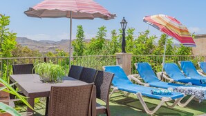 A terrace with wicker furniture, striped umbrellas, and a view of the countryside. - Ta Danjela Villa Sleeps 8 With Pool (Xaghra)