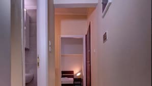 Ein schmaler Korridor mit Holzboden, der zu einem Schlafzimmer mit Bett und Nachttisch führt.