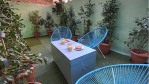 Eine kleine Terrasse im Freien mit Tisch und Stühlen, umgeben von Blumentöpfen.