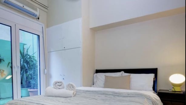 Ein Schlafzimmer mit Bett, Nachttisch, Lampe und Blick ins Freie.