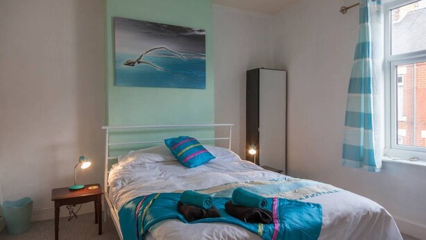 A bedroom with a bed, a nightstand, a lamp, a wardrobe, and a window with curtains. - House - Sleeps 4 - Pets Ok - Parking - Garden (Guisborough)