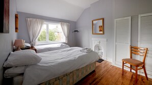 Une chambre avec deux lits, une chaise en bois, une table de chevet avec une lampe et une fenêtre avec des rideaux.