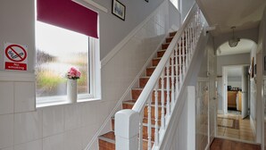 Un escalier avec des rampes blanches et des marches en bois, menant à une pièce dotée d’une fenêtre et d’un panneau indiquant « Il est interdit de fumer ».