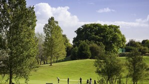 Un parcours de golf avec un fairway herbeux, des arbres et quelques personnes qui jouent.