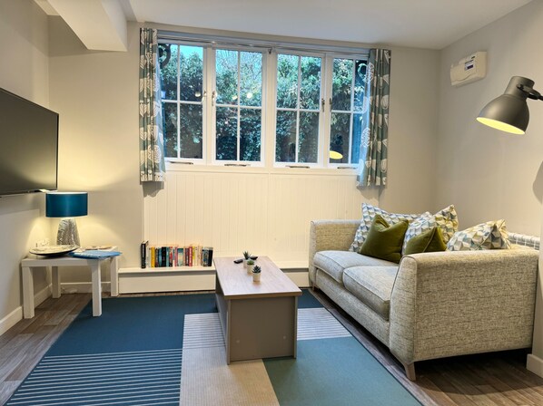 A living room with a sofa, a coffee table, a TV, and a window with curtains. - Warehouse Apartments (Ulverston)