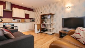 A modern living room with a sofa, a television, and a kitchen area with cabinets and appliances. - Luxury 1bedroom Lodge in Prestwich (Manchester)