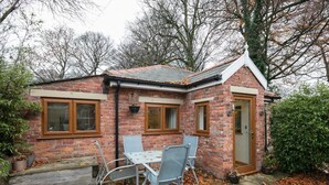 A small brick house with a tiled roof, a wooden door, and a window. There is a table and two chairs outside. - Luxury 1bedroom Lodge in Prestwich (Manchester)