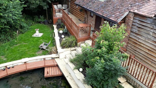 Une cabane en bois avec une terrasse, un petit jardin et un étang.