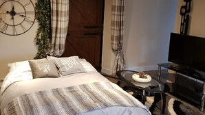 Une chambre à coucher avec un lit, une horloge, un téléviseur et une petite table sur laquelle se trouve un bol de fruits.