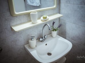 A bathroom with a white sink, a mirror, and a shelf with a soap dish and a potted plant. - Babalogo Apartments (Hersonissos)